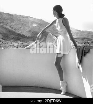 Mannequin de mode portant un ensemble de tennis, portrait en longueur assis sur un mur avec montagnes en arrière-plan, photo de Toni Frissell, février 1947 Banque D'Images