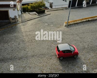 Vue de dessus d'une voiture rouge compacte qui roule sur des galets rue en pierre Banque D'Images