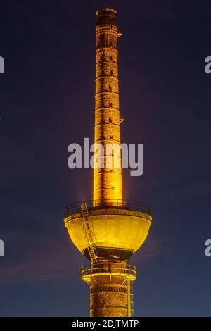 Ancienne cheminée de brique de l'usine illuminée de lumière dorée la nuit Banque D'Images