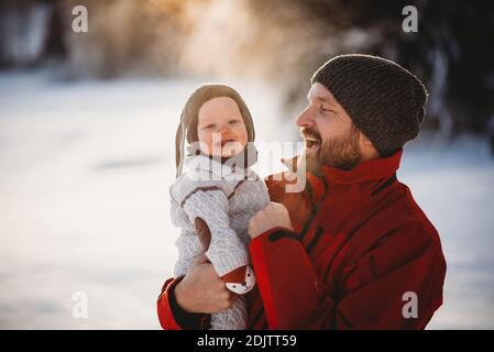 Père tenant un bébé souriant dehors dans la neige en Scandinavie Banque D'Images