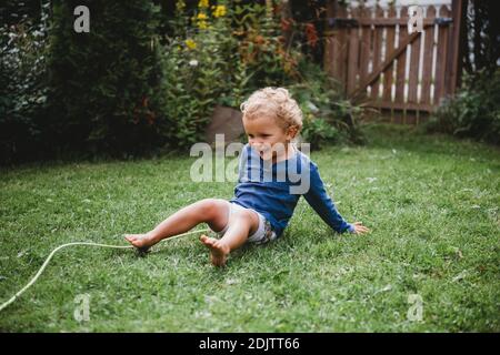 Petit garçon jouant dans la baykyard en été ayant plaisir assis sur l'herbe Banque D'Images