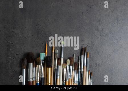 Une rangée de pinceaux d'artiste de divers modèles se trouve sur une surface en stuc sombre et décorative avec un espace de copie. Banque D'Images