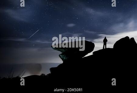 Un homme regarde un météore pendant la douche de météores de Geminid au-dessus de Brimham Rocks, une collection de formations rocheuses d'équilibre dans la région de Niddover de beauté naturelle exceptionnelle dans le North Yorkshire. Banque D'Images