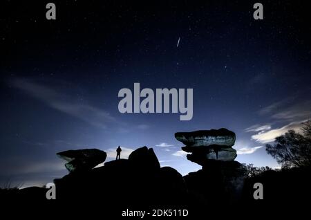 Un homme regarde un météore pendant la douche de météores de Geminid au-dessus de Brimham Rocks, une collection de formations rocheuses d'équilibre dans la région de Niddover de beauté naturelle exceptionnelle dans le North Yorkshire. Banque D'Images