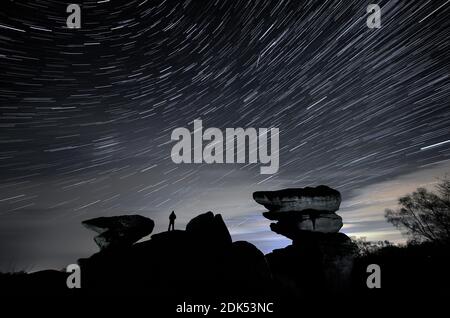 LES ÉDITEURS NOTENT L'EFFET CRÉÉ EN SUPERPOSANT PLUSIEURS IMAGES TOURNÉES CONSÉCUTIVEMENT À PARTIR D'UN SEUL APPAREIL PHOTO UN homme regarde un météore pendant la douche du météore Geminide au-dessus de Brimham Rocks, une collection de formations rocheuses d'équilibrage dans la région de Niddnaturelle de beauté exceptionnelle dans le North Yorkshire. Banque D'Images