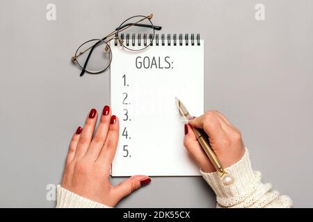 La main féminine tient le stylo et écrit le texte 2021 objectifs du nouvel an sur le bloc-notes blanc sur fond gris vue du dessus Flat Lay motivation d'affaires, idée, succès Banque D'Images