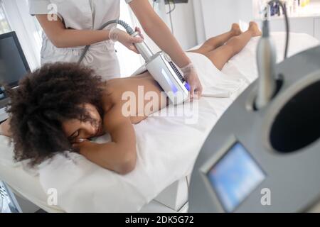 Session de correction laser. Jeune fille aux cheveux foncés avec des yeux fermés allongé sur un canapé à l'estomac recevant une séance de correction laser Banque D'Images