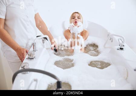Femme sereine soufflant de la mousse des mains dans le bain Banque D'Images