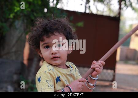 Un petit enfant indien regardant la caméra qui tient un bâton de bois Banque D'Images