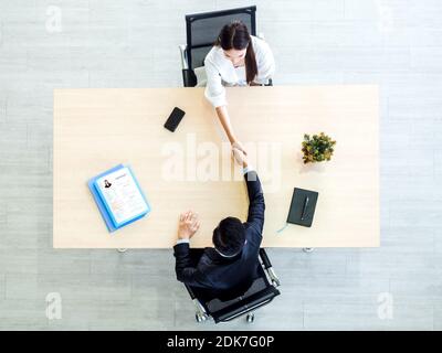 Vue en grand angle d'un homme d'affaires en costume en train de secouer la main avec une candidate sur un bureau en bois avec des papiers de CV ou de CV dans le bureau. Entretien d'emploi, affaires, Banque D'Images