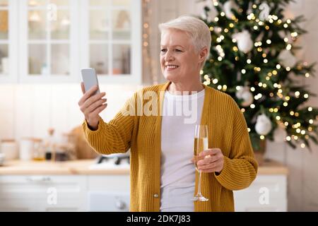 Belle grand-mère ayant la fête en ligne au téléphone pendant la célébration de Noël Banque D'Images