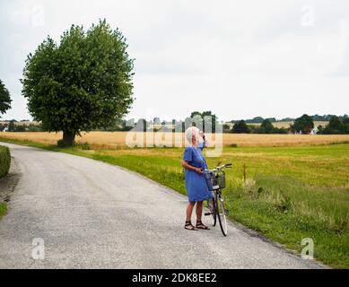 Femme âgée avec vélo par champ Banque D'Images