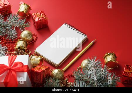 Bloc-notes et crayon pour écrire des voeux et des cadeaux pour le nouvel an et Noël autour des décorations d'arbre de Noël sur un fond rouge. Nouvel an moo Banque D'Images