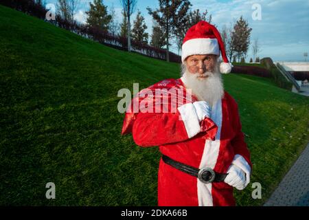 Drôle de Père Noël portant le costume rouge dans des verres debout dans la rue Banque D'Images