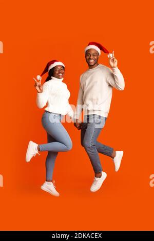 Couple noir espiègle à Santa Hats tenant les mains et montrant Geste de paix Banque D'Images