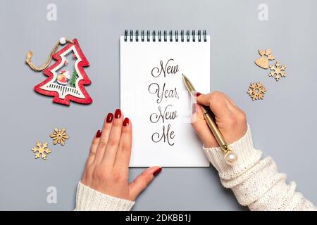 La main féminine tient un stylo et écrit New Year, New Me sur bloc-notes blanc, arbre, flocon de neige sur fond gris vue du dessus Flat Lay motivation d'affaires, idée Banque D'Images