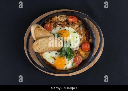 petit déjeuner sain shakshuka - oeufs frits, oignon, poivron, tomates et épices dans un stewpan en fonte sur une ancienne planche en bois. Banque D'Images