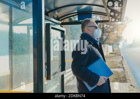 Man se tient à l'arrêt de bus qui attend le bus dans un masque antiviral Banque D'Images