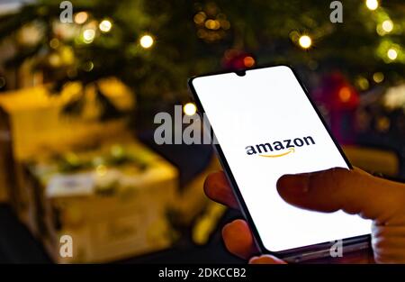 Application Amazon, application shopping en ligne, icône affichée sur le smartphone avec le doigt, sapin de Noël et cadeaux en arrière-plan Banque D'Images