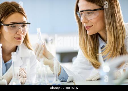 Deux jeunes chercheuses scientifiques qui regardent des flacons avec solutions dans un laboratoire Banque D'Images