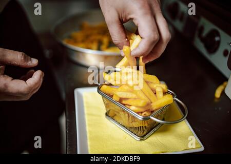 Gros plan des mains du chef qui organisent les frites dans un petit panier métallique au restaurant. Prêt à servir Banque D'Images
