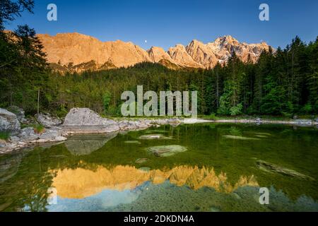 Reflet du massif du Wetterstein dans les Alpes allemandes, pendant la lumière du soir et trois quarts de lune dans un petit lac près de l'Eibsee. En arrière-plan le Zugspitze. Banque D'Images