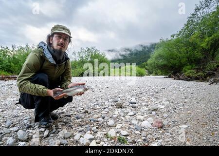 Après le rinçage de la centrale hydroélectrique de Krün, l'Isar est tombé complètement à sec dans certains endroits. De petites et grandes truites, des cocs et de nombreux autres petits animaux sont morts. Autoportrait avec truite morte trouvée. Banque D'Images