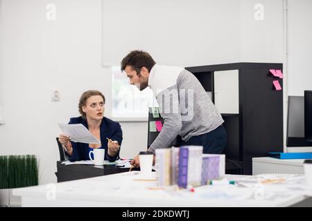 Une femme superviseur expliquant quelque chose à un gars de son personnel. Le membre de l'équipe écoute attentivement le document auquel il se penche. Banque D'Images