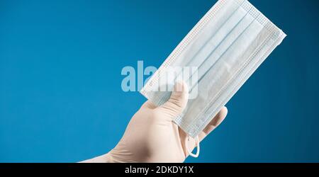 masque dans la main du médecin avec gant chirurgical et fond bleu. Banque D'Images