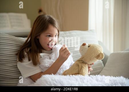 Mignon, malade fille joue docteur, mesure la fièvre d'un ours en peluche. Banque D'Images