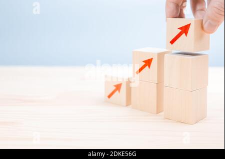 Gros plan homme d'affaires main arranger le cube en bois avec flèche empilant comme escalier. Schéma de carrière de l'échelle pour la croissance de l'entreprise processus de réussite concept.main a Banque D'Images