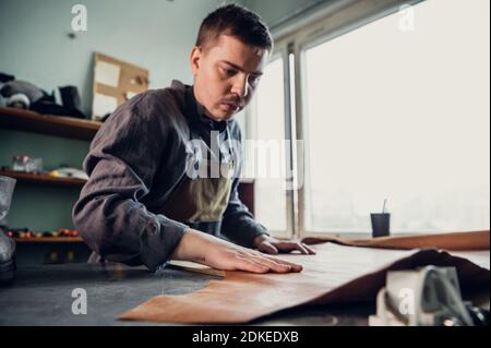 Un jeune cordonnier commence à fabriquer des chaussures, pose un rouleau de cuir sur la table. Banque D'Images