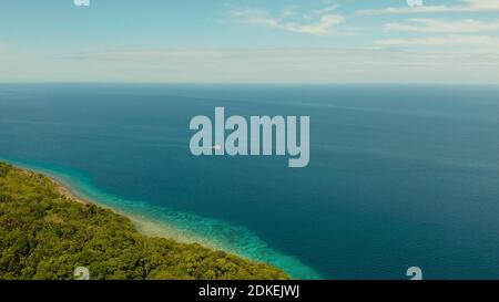 Littoral de forêt et de palmiers, avec des récifs coralliens d'eau turquoise, vue aérienne. Seascape tropical de l'île couverte de forêt verte contre le ciel bleu avec les nuages et la mer bleue Banque D'Images