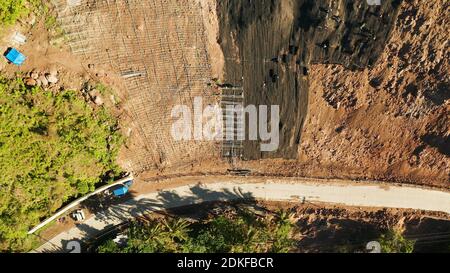 Renforcer les travailleurs la pente de la montagne avec le grillage de métal prévenir les chutes de pierres et glissements de terrain sur la route, vue ci-dessus. Les travailleurs de la construction de mur de béton anti-glissement prévenir protéger contre les glissements rocheux concept de sécurité. Banque D'Images