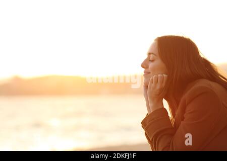 Profil d'une femme avec les yeux fermés au coucher du soleil relaxant l'esprit sur la plage en hiver