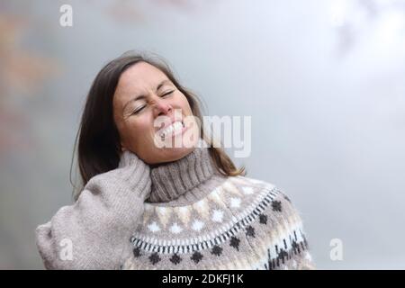 Femme d'âge moyen souffrant de mal de cou dans un froid et journée d'hiver brumeuse Banque D'Images