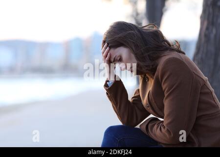 Profil d'une triste femme se plaignant assise sur un banc en hiver sur la plage