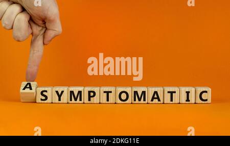 Covid-19 asymptomatique ou symptomatique. La main mâle tourne des cubes et change le mot 'smptomatic' en 'asymptomatique'. Magnifique arrière-plan orange. Médical Banque D'Images