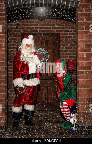 Royaume-Uni, Quorn - décembre 2020 : le Père Noël et un Elf se faufilent devant une porte, dans la neige, comme ils livrent des cadeaux Banque D'Images