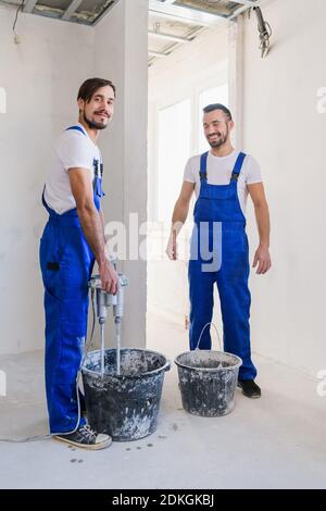 Deux ouvriers en uniforme bleu préparent le ciment dans un seau Banque D'Images