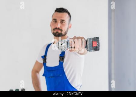 L'ouvrier en uniforme regarde la caméra et montre le foret Banque D'Images