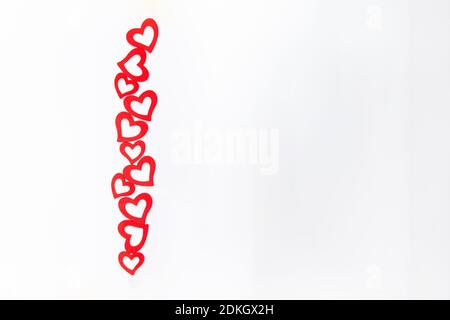 Une rangée verticale de coeurs en bois rouge découpé sur un fond blanc. Toile de fond de Saint-Valentin Maquette de carte de vœux Happy Lovers Day. Pose à plat. Mise au point sélective Banque D'Images