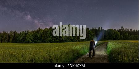 Photo panoramique d'un homme avec son vélo en regardant le la beauté de la milkyway au ciel nocturne sombre à la campagne Banque D'Images