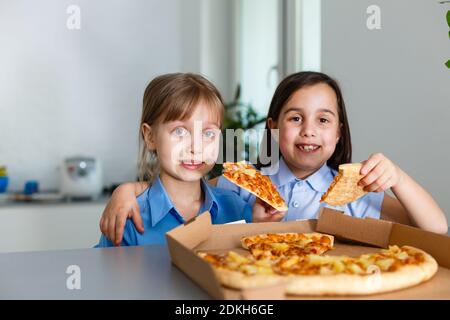 Deux petites filles amies joyeuses qui mangent des tranches de pizza. Banque D'Images