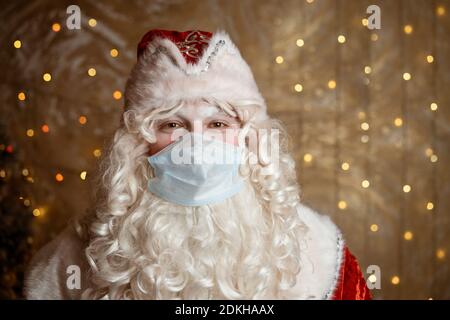 Le Père noël dans un masque médical sur fond de mur avec bokeh des guirlandes Banque D'Images