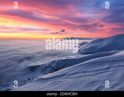 Majestic sky with pink cloud. Fantastic sunrise illuminates the mountain, thick fog and horizon. Snowy winter morning. Wallpaper background. Location Stock Photo