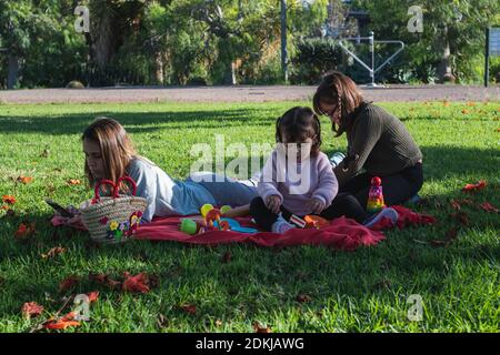 Mère et fille sur une couverture rouge sur l'herbe, dans le parc, jouant pique-nique avec leurs jouets Banque D'Images