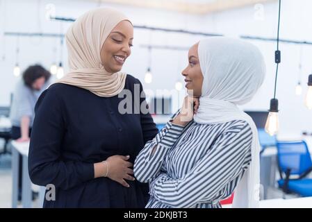 Portrait de deux femmes d'affaires afro-américaines qui discutent entre elles tout en étant debout dans un bureau d'affaires moderne avec leurs collègues, collègues dans le TH Banque D'Images