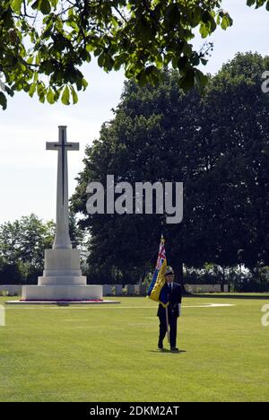 Un ancien combattant britannique marche avec un drapeau de la Croix du sacrifice au cimetière de la Commission des sépultures de guerre du Commonwealth de Bayeux, à Bayeux, en France. Banque D'Images