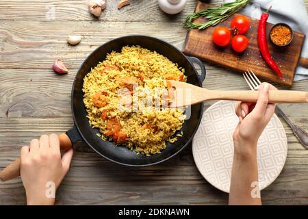 Femme mettant pilaf dans l'assiette de la poêle sur bois tableau Banque D'Images